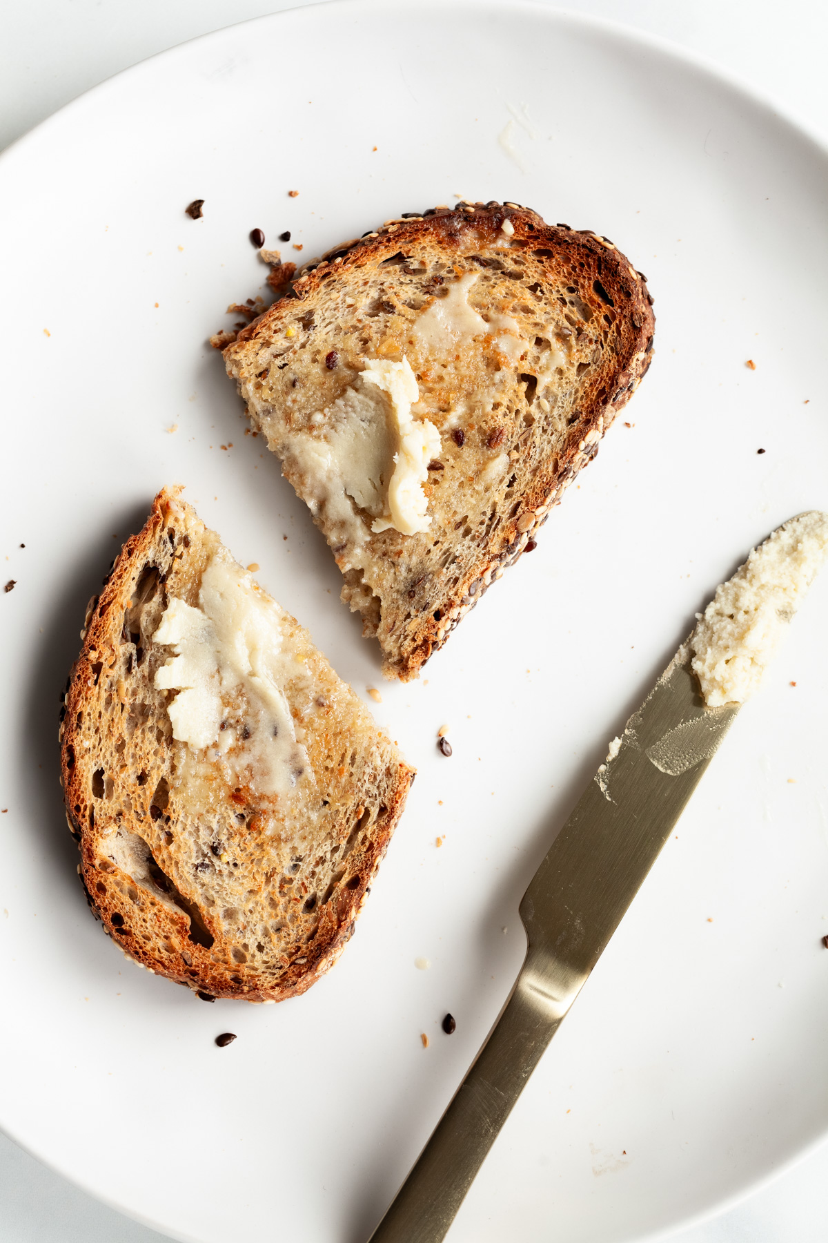 overhead view of two slices of toast with butter and a butter knife on a white surface with crumbs.