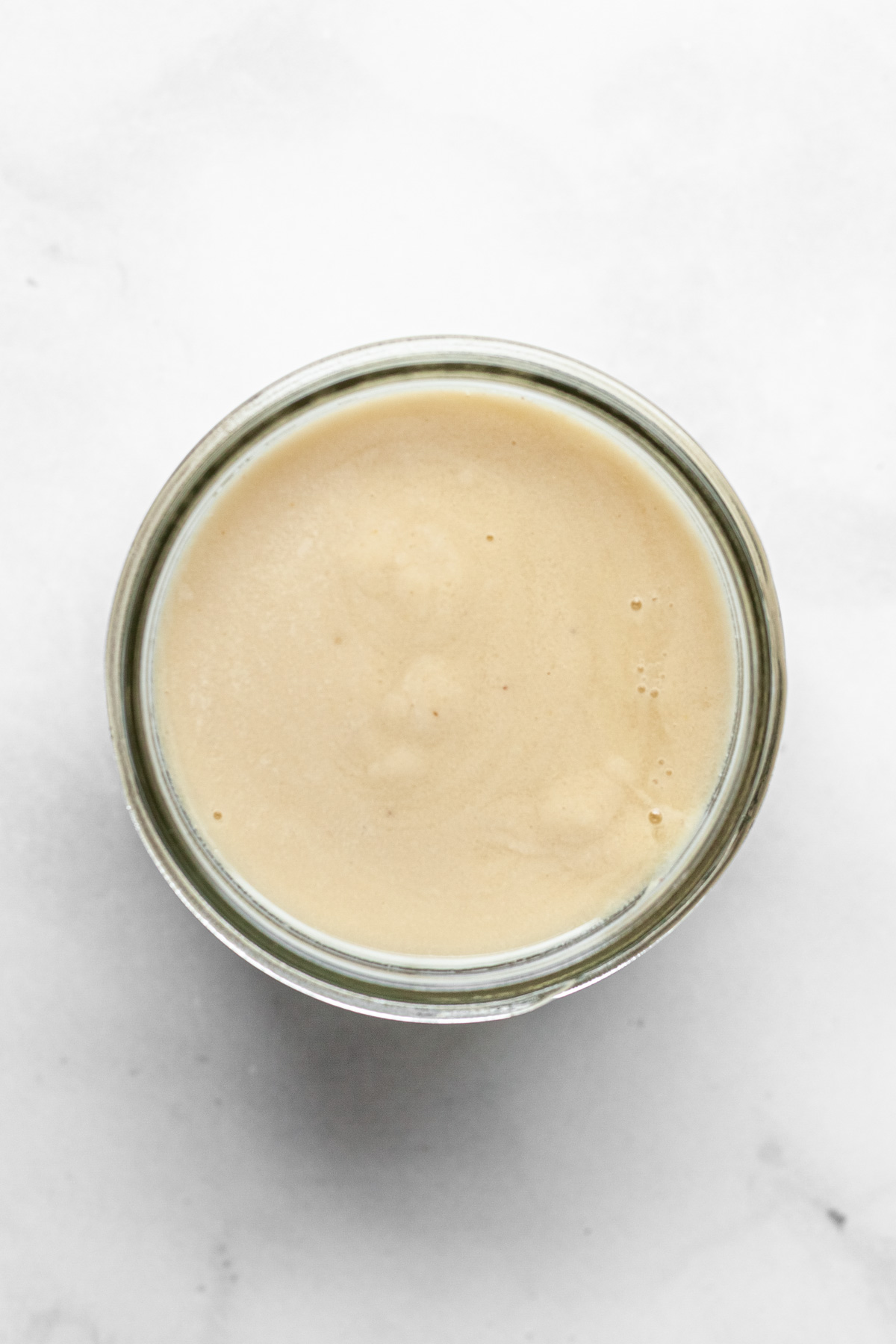 an overhead view of un-solidified vegan butter in a glass jar on a white surface.