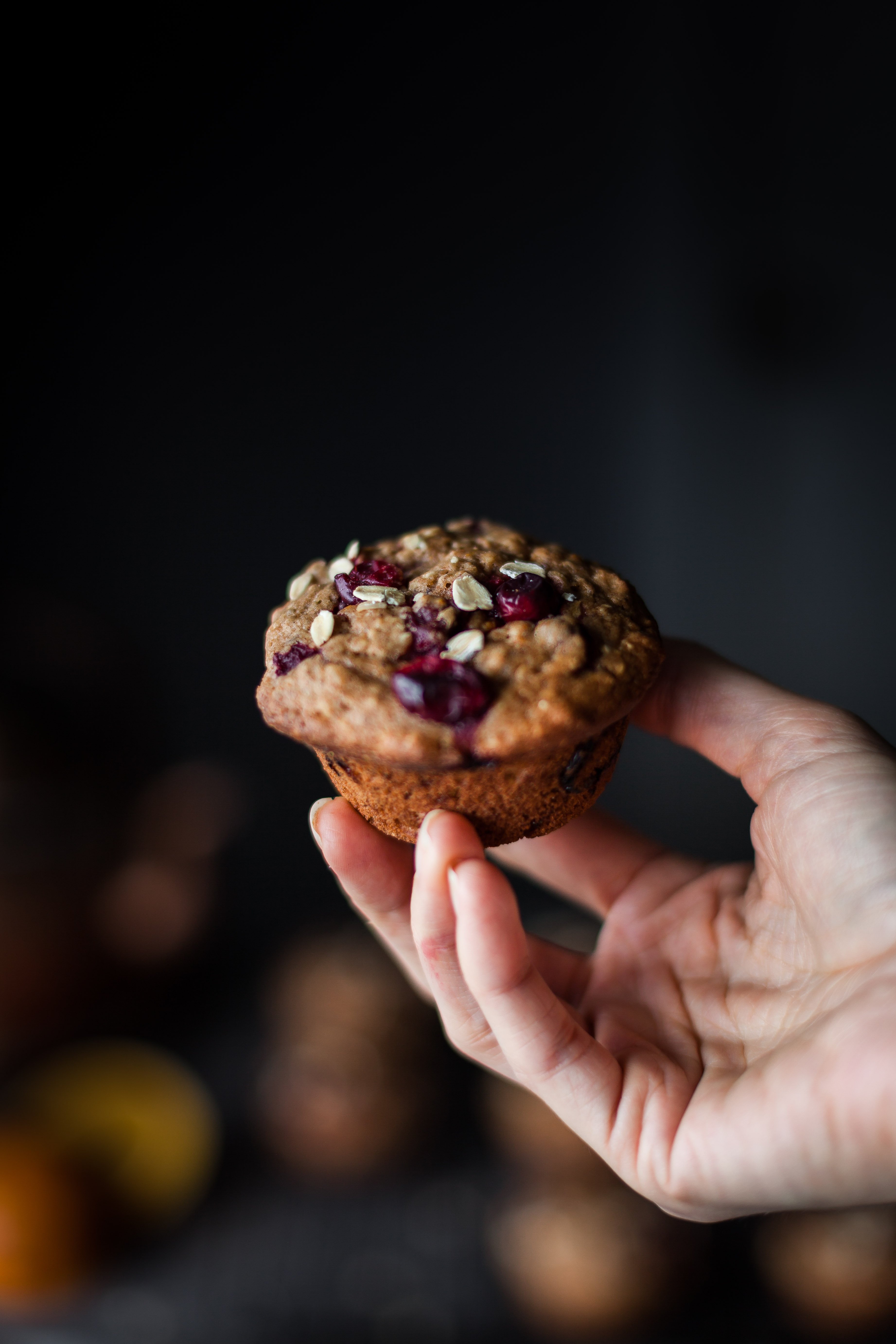 a hand holding a cranberry citrus oat muffin.