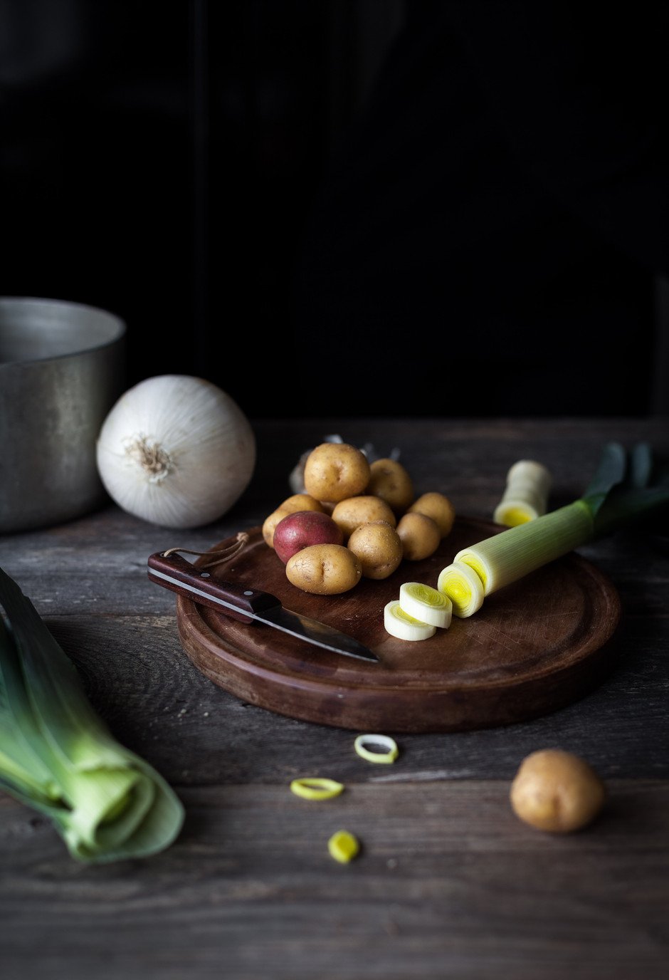 portrait of sliced leeks and potatoes on a cutting board with a knife. 