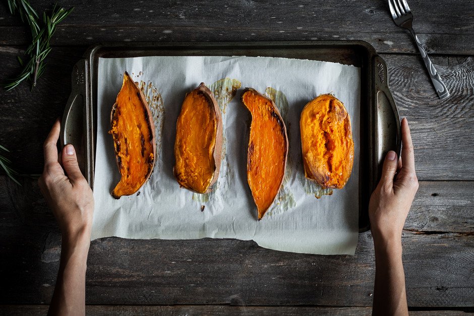 overhead of hands holding a tray of 4 sweet potatoes.