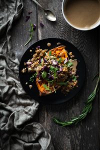 overhead of a stuffed sweet potato on a black plate with a linen and bowl of dressing with a spoon.