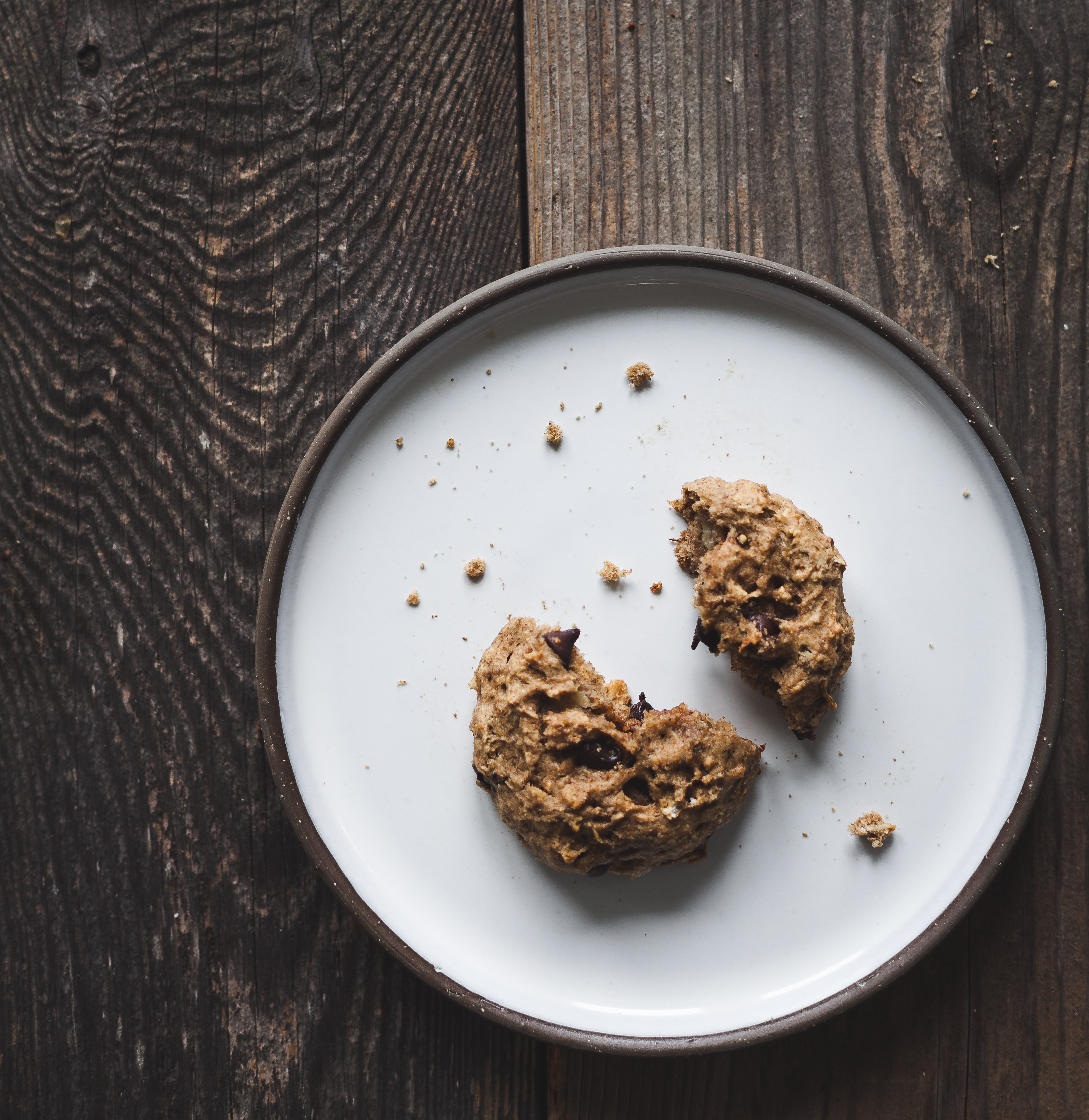 an overhead image of a broken cookie on a white plate on a wood surface.