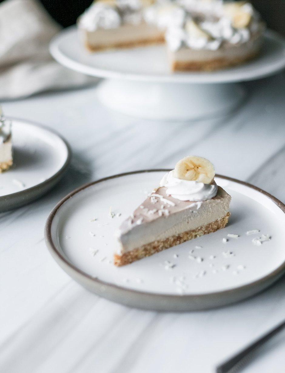 a slice of vegan banana cream pie on a white plate on a white surface.