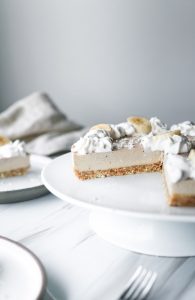 a banana cream pie on a white cake stand with a slice missing.