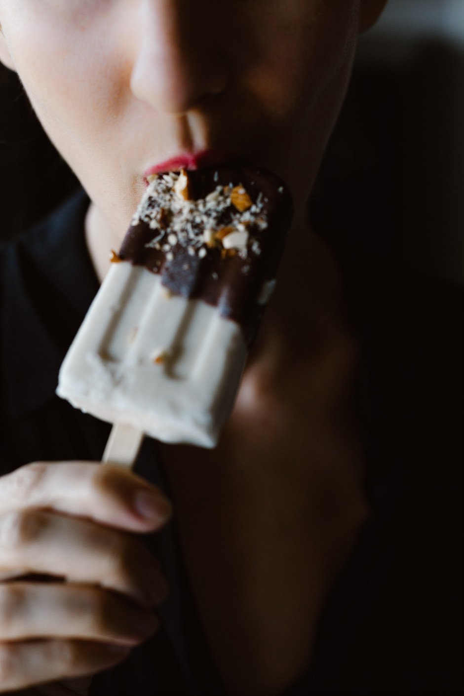 a close up of a person biting into an ice cream bar.
