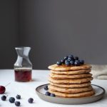 a stack of pancake with blueberries and a jar of syrup.