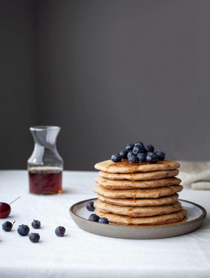 a stack of pancake with blueberries and a jar of syrup.
