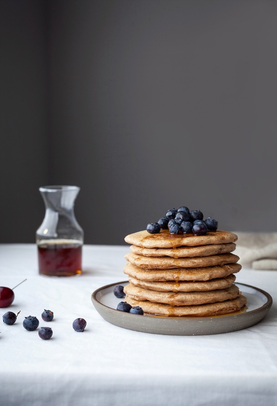 a stack of pancakes with blueberries ontop with maple syrup in a small jar. 