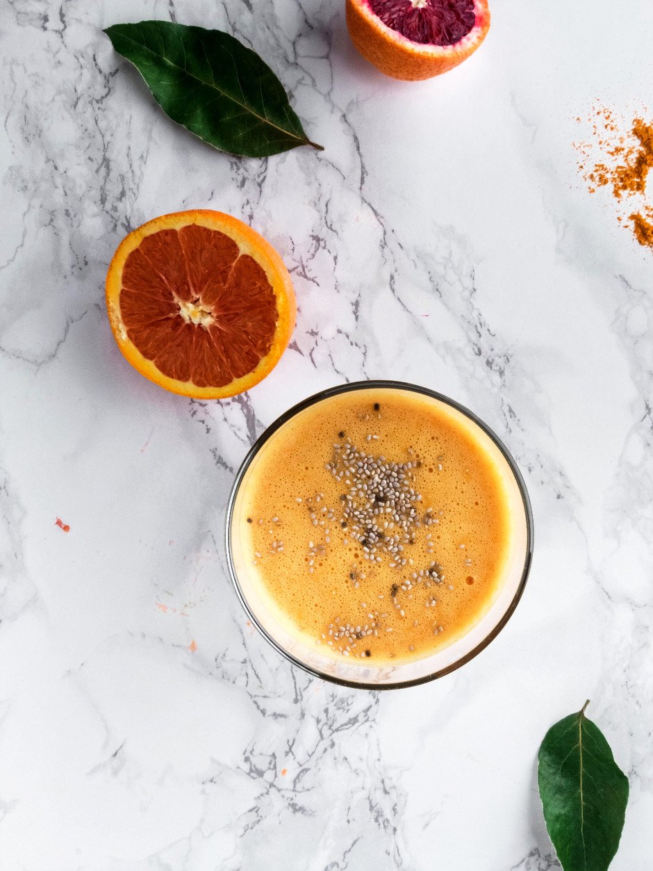 Overhead image of orange slices, turmeric and a citrus and root sunshine smoothie on a white surface. 