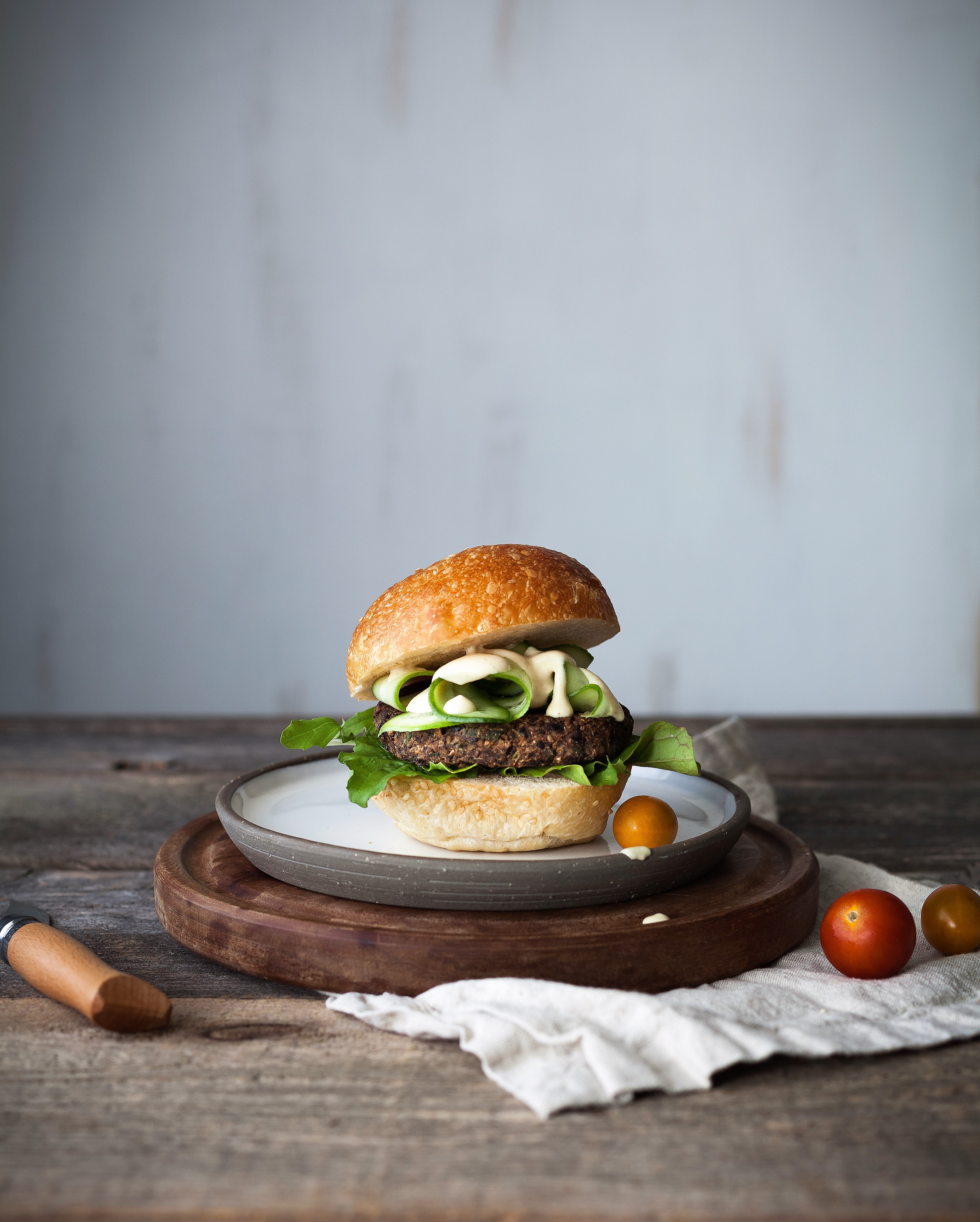 a portrait of a veggie burger on a cutting board with cherry tomatoes and a biege linen.
