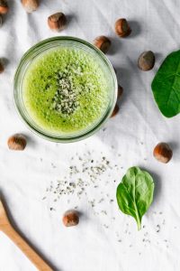 overhead of a green smoothie on a white surface with hazelnuts and spinach.