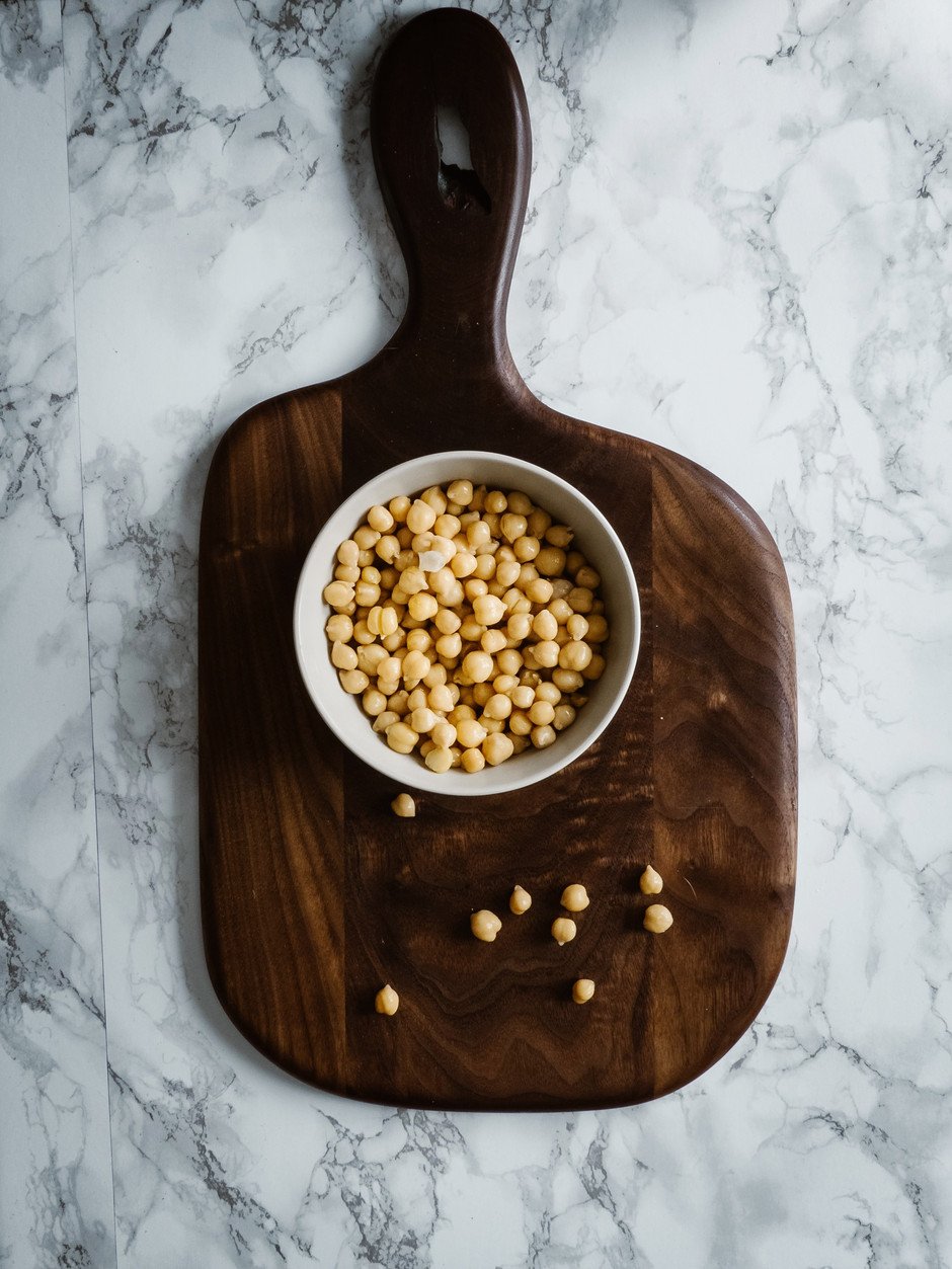 an overhead image of  a bowl of chickpeas on a wooden cutting board.