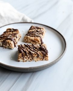 close up portrait of three vegan salted caramel granola bars on a white plate on a white surface with a beige linen on the left.