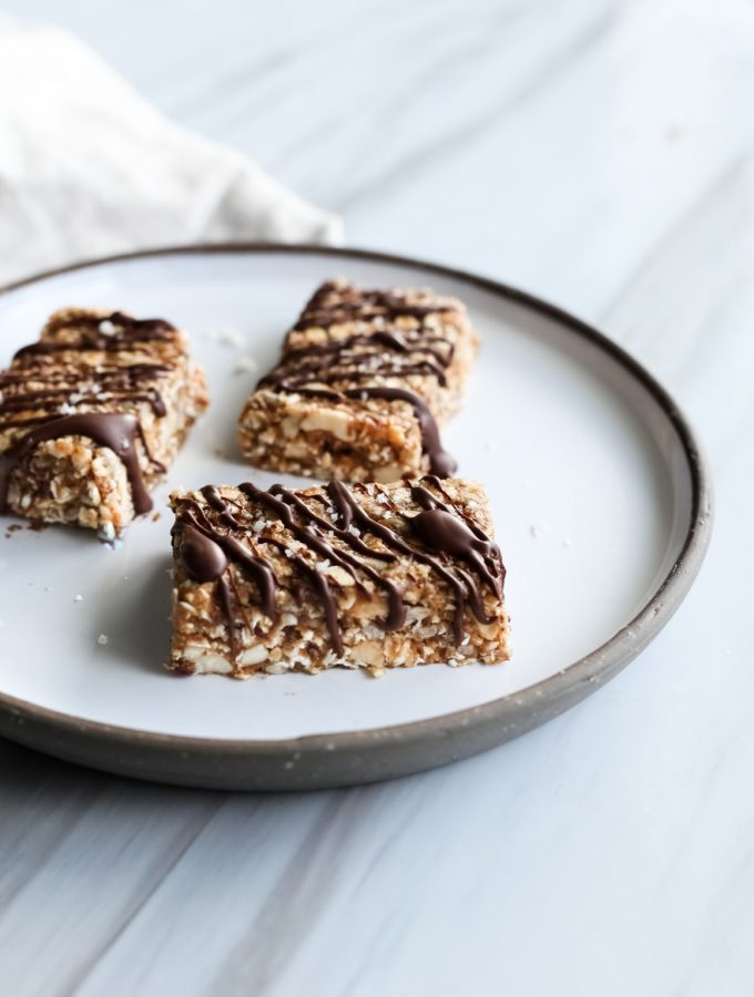 close up portrait of three vegan salted caramel granola bars on a white plate on a white surface with a beige linen on the left.