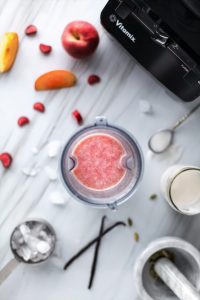 overhead view of a peach lassi in a glass with ice, peaches and a blender.