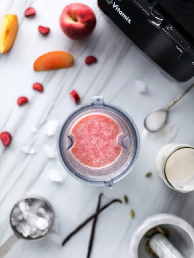 overhead view of a peach lassi in a glass with ice, peaches and a blender.