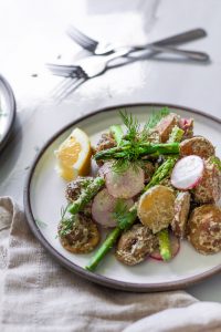 angled view of a plate of potato salad on a white surface.