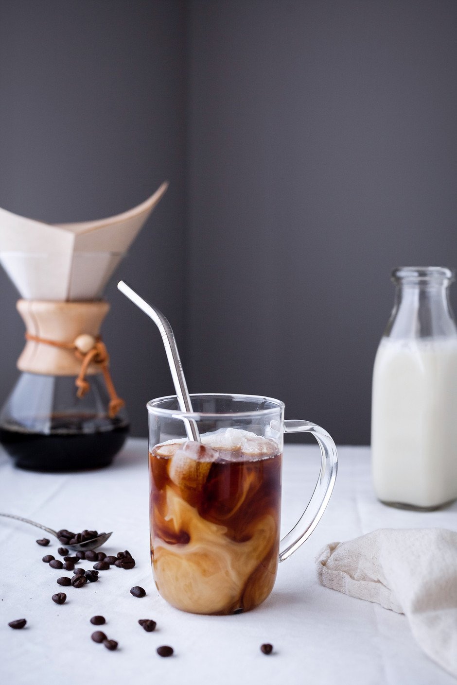 a head on image of a cup of cold brew coffee with a chemex coffee maker in the background with a jug of almond milk. 