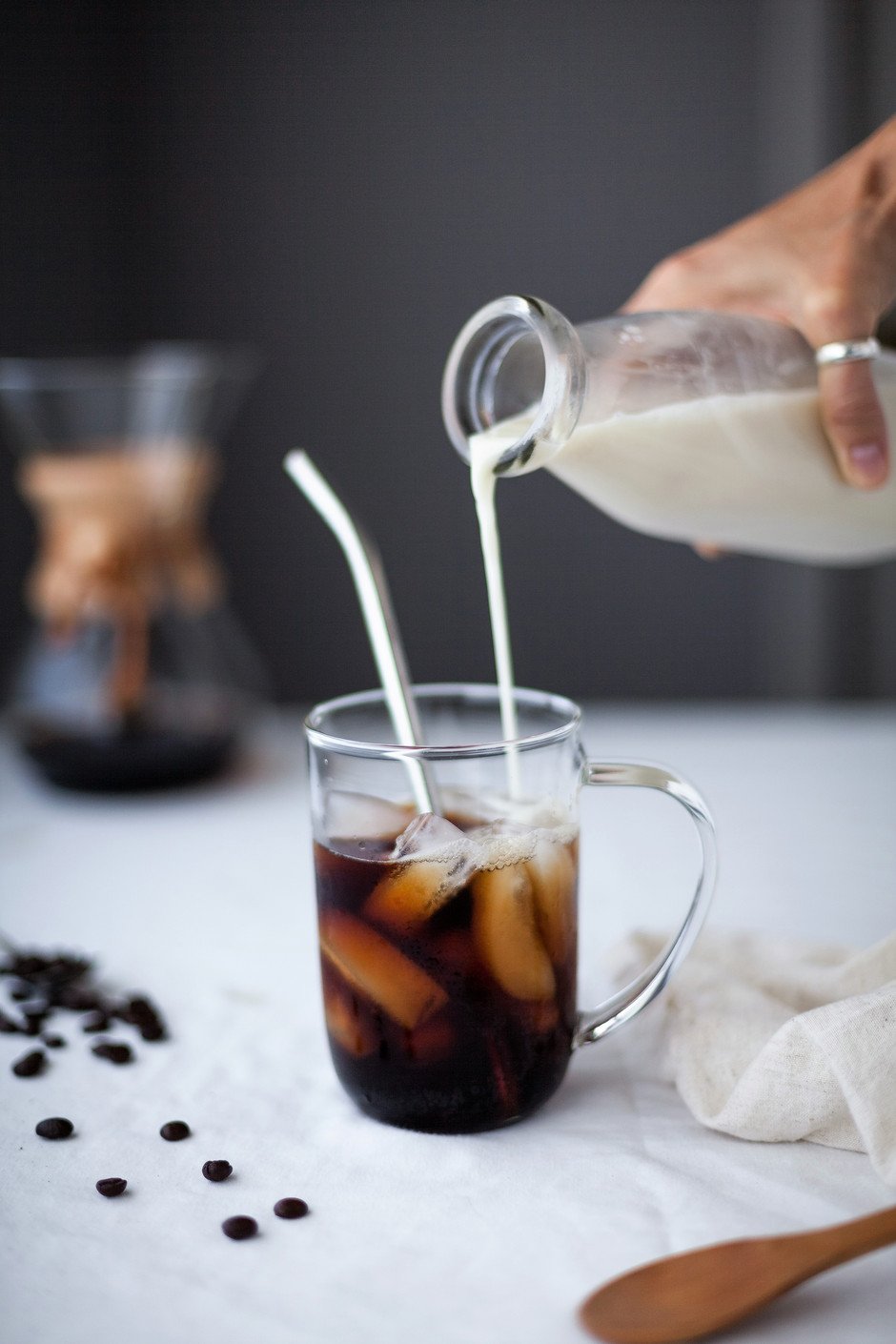 head on image of almond milk being poured into a glass of cold brew coffee with a straw.