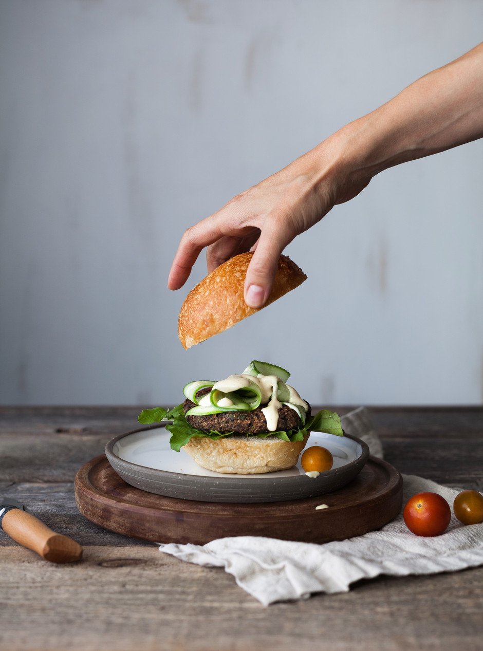 portrait of a hand putting placing a burger bun top on a burger.