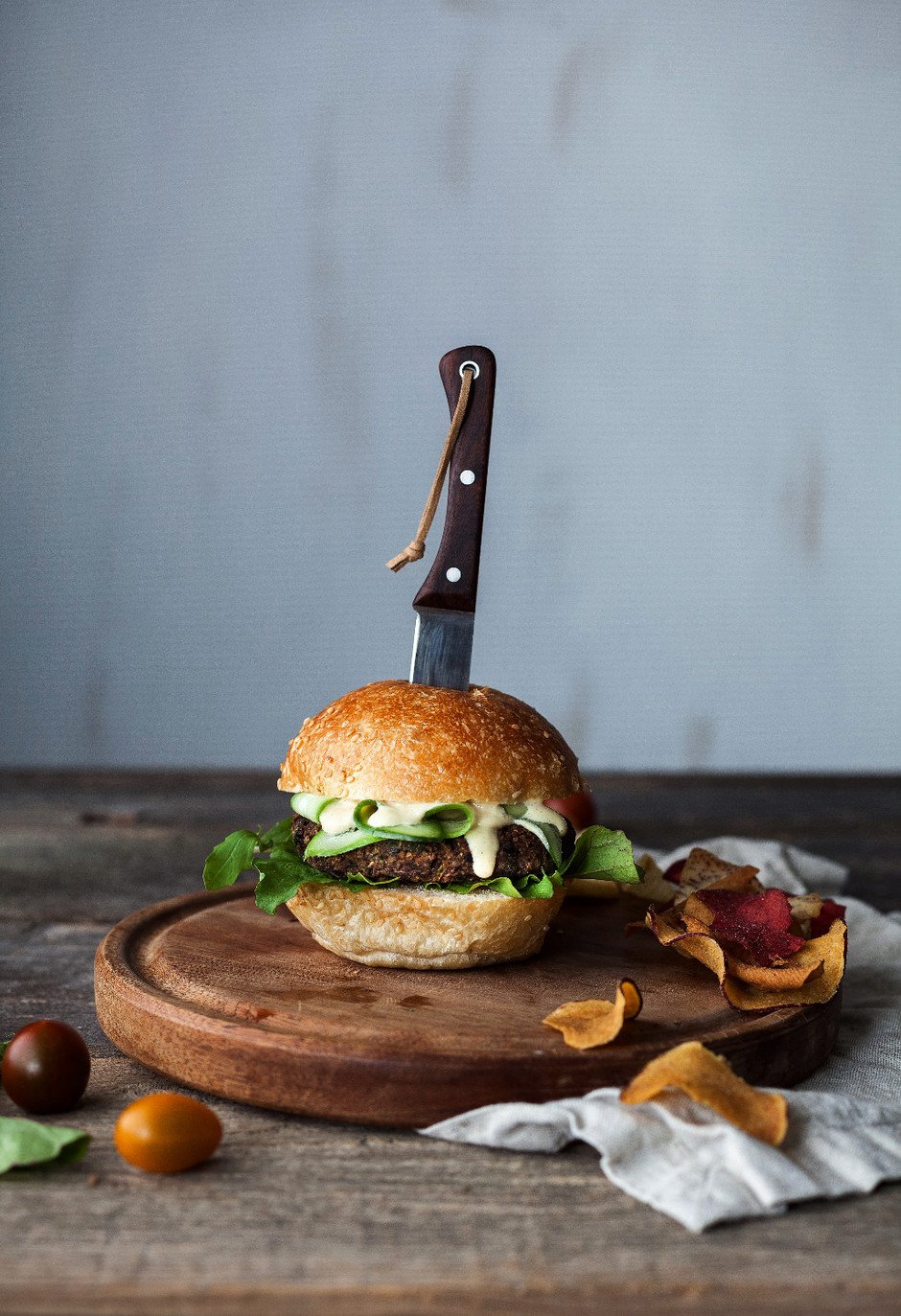 a portrait of a veggie burger on a cutting board with a knife through it.