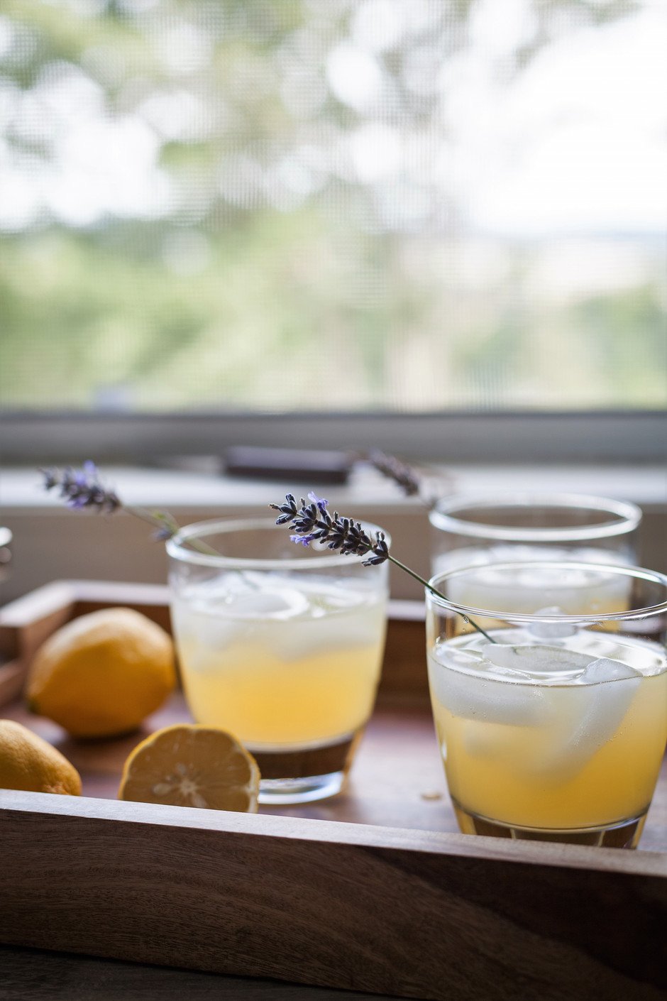 three glasses of schorle on a tray next to a window with lavender sprigs and lemons. 
