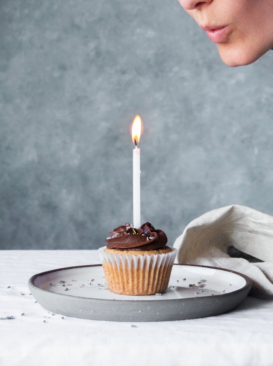 a person blowing out a candle on a frosted cupcake.