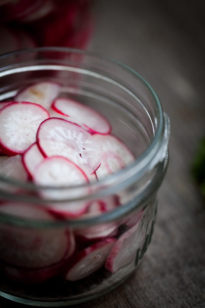 close up portrait of slices radishes in a glass jar.