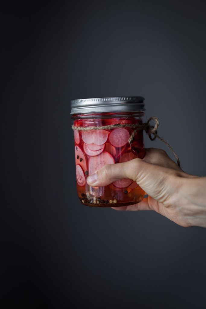 A hand holding a jar of pickled radishes with twine tied around the top.