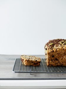 side view of harvest apple crunch loaf on a cooling rack with a slice cut off.