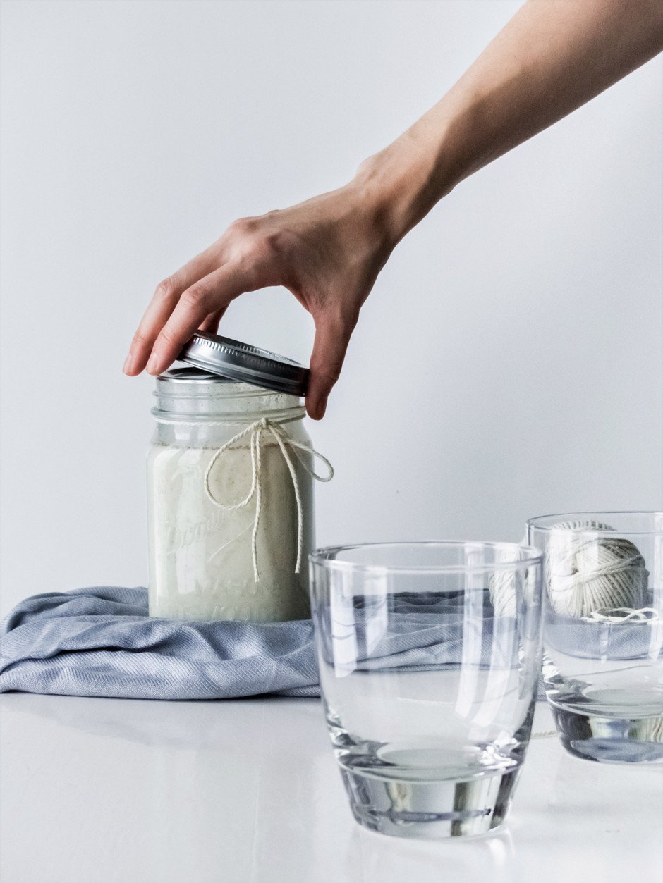 a head on image of a person unscrewing a lid of vegan egg nog with two empty glassess in the foreground.