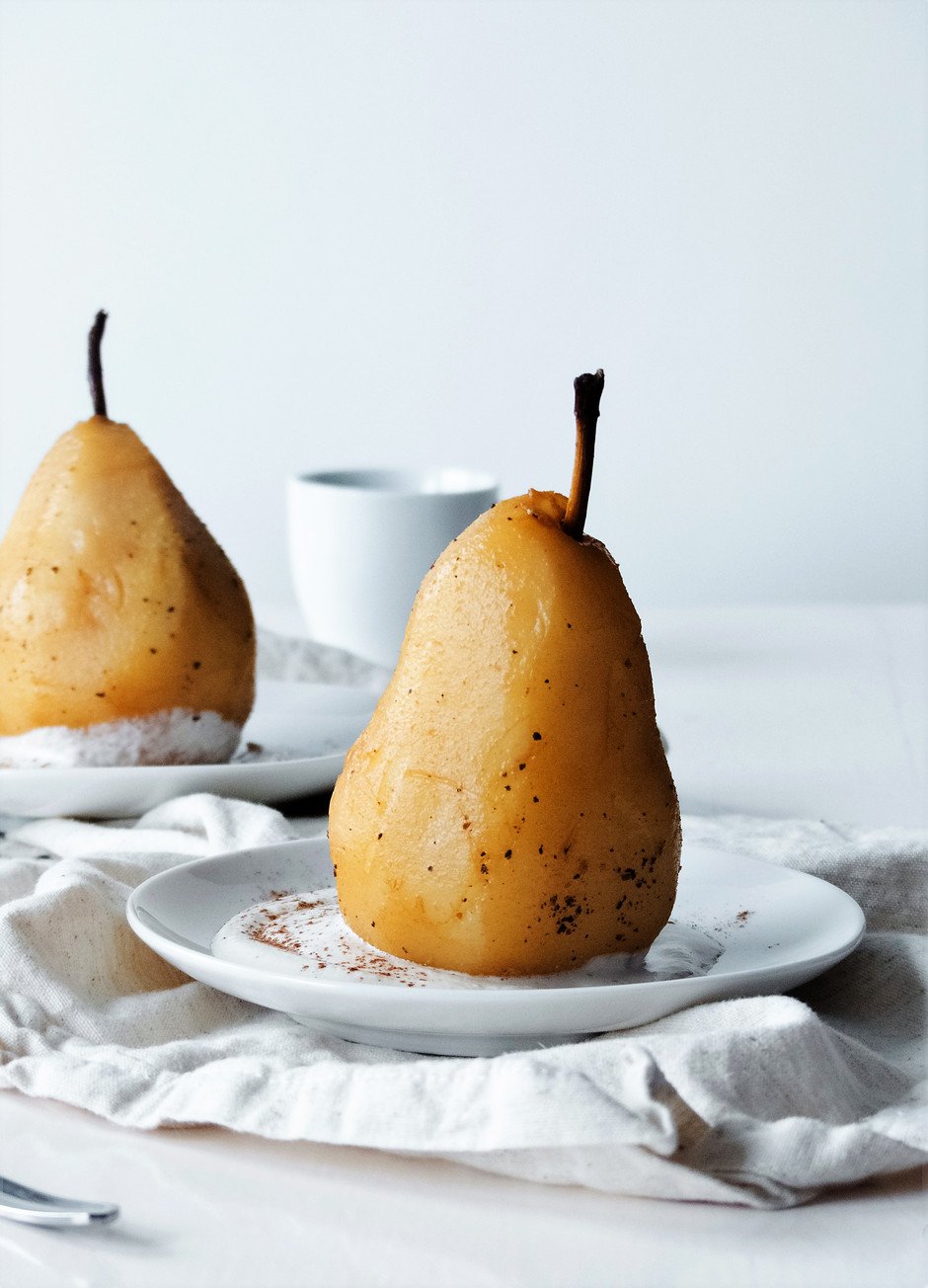 a straight on close up image of a Chai Poached Pear on a white plate against a white background.