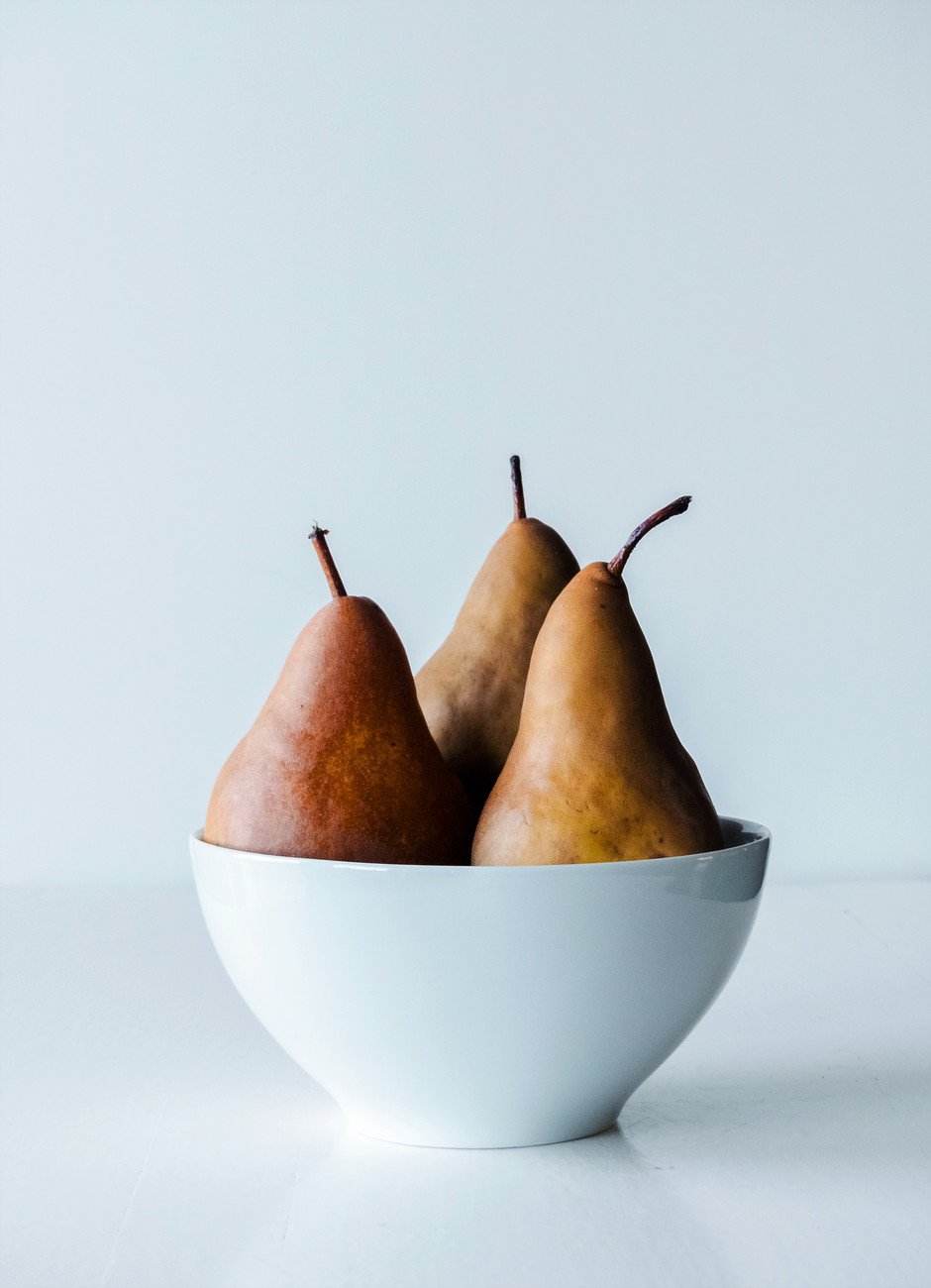 a straigh on image of three bosc pears in a white bowl against a white background.