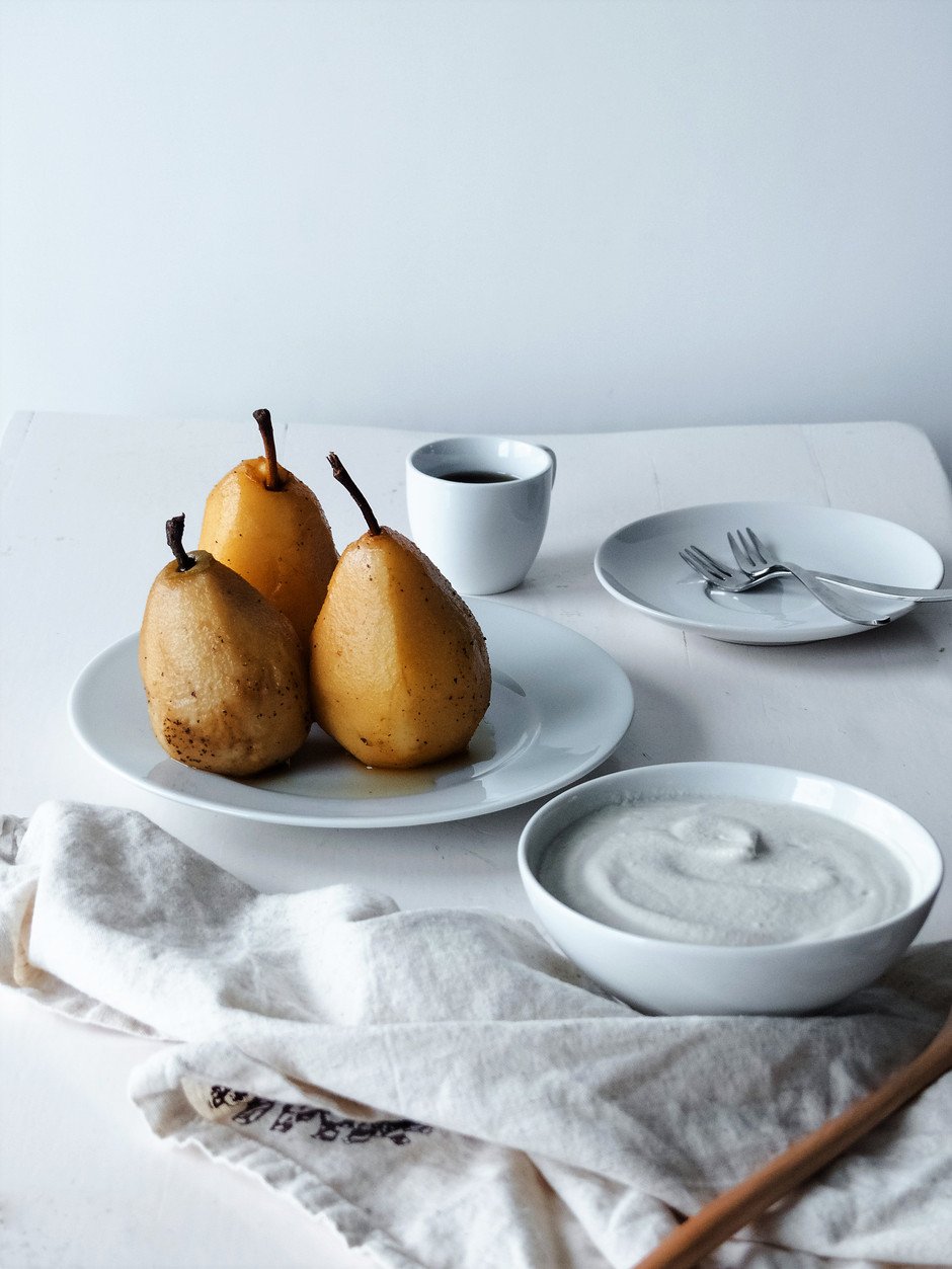 A straight on image of three Chai Poached Pears sitting on a white plate with white dishes off to the side.