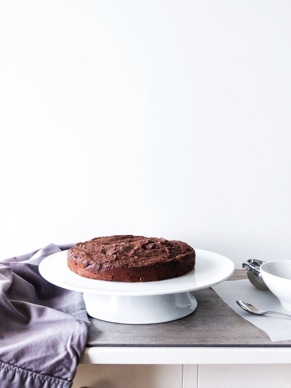 A straight on image of a chocolate torte sitting on a white cake stand against a white background.