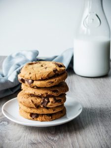 a stack of chocolate chip cookies with a blue linen and jar of milk in the background.