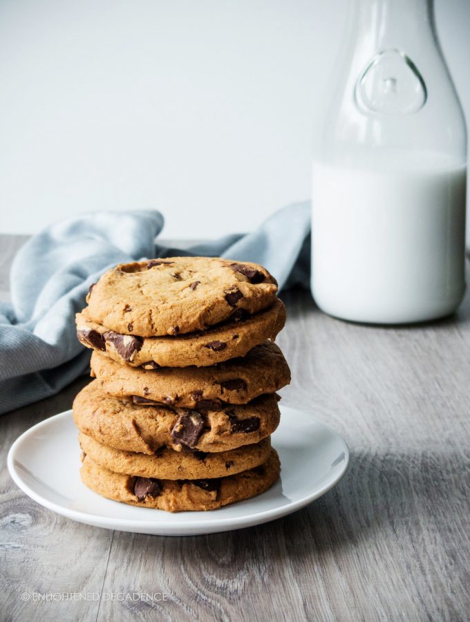 a stack of chocolate chip cookies with a blue linen and jar of milk in the background.