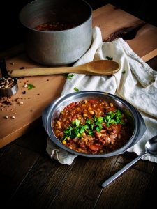 a bowl of bean soup with a wooden spoon, linen, and pot.