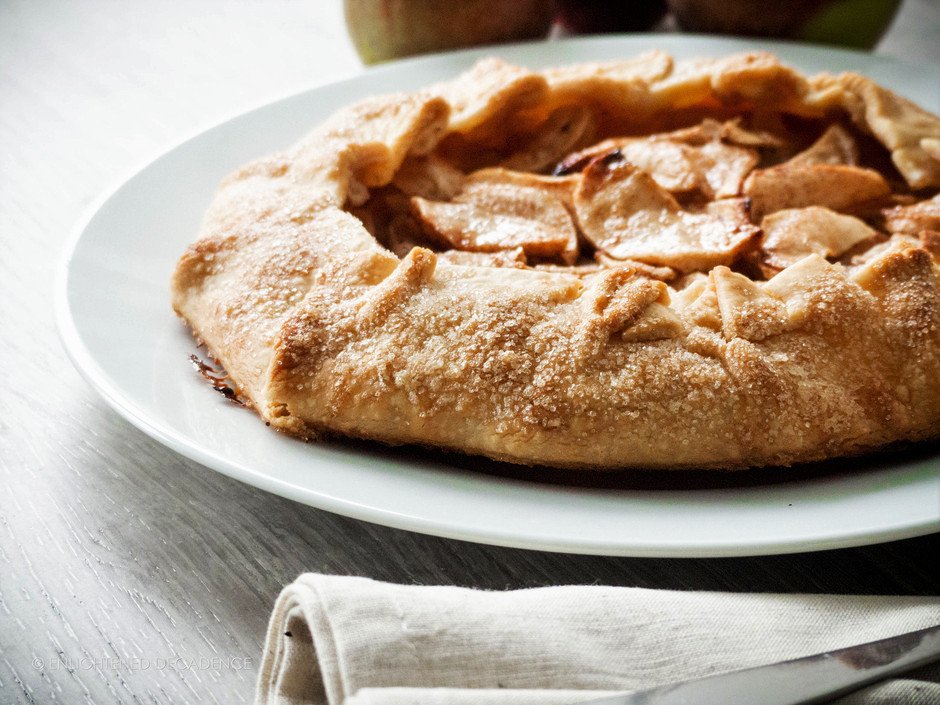 a head on image of an apple galette sitting on a white plate with a linen napkin in the foreground. 
