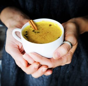two hands cupping a mug of golden milk with a cinnamon stick.