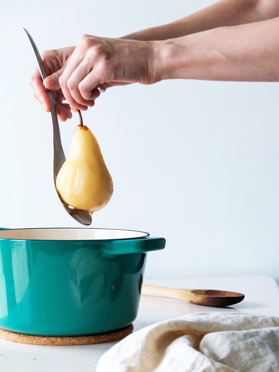 a straight on image of a person taking a poached pear out of the poaching liquid with a spoon.