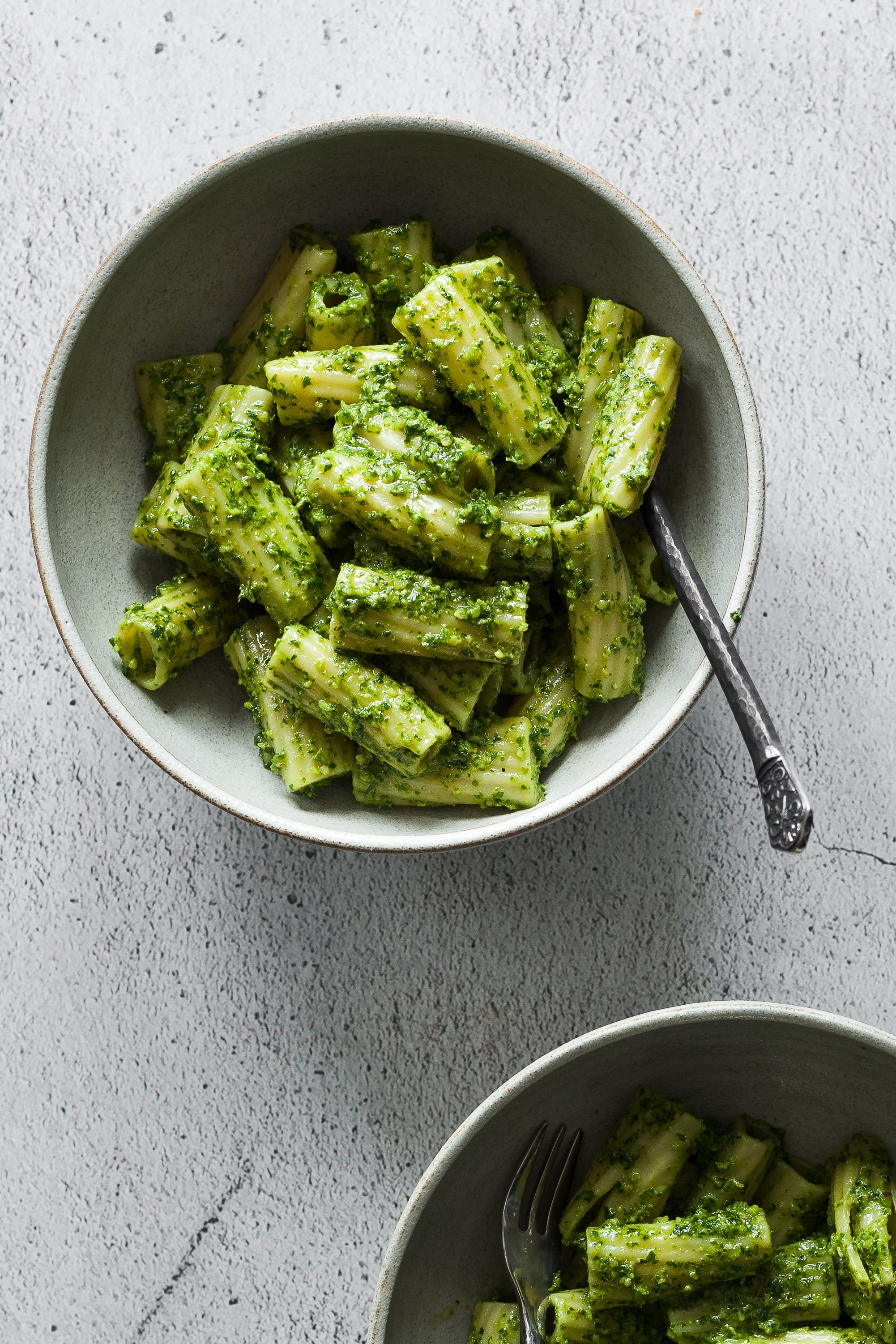an overhead close up image of a bowl of vegan parsley walnut pesto pasta on a white stone surface.