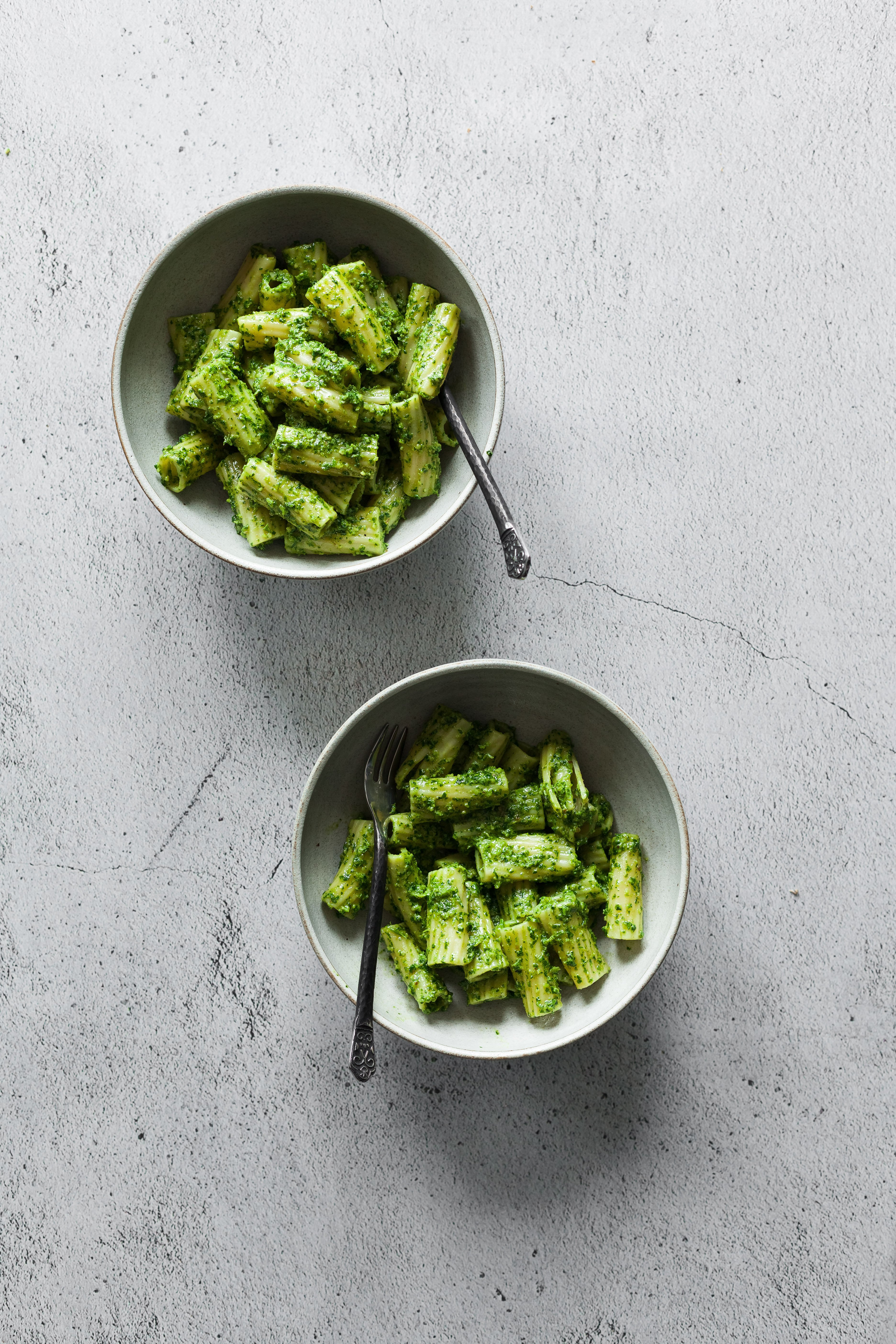 an overhead image of two bowl of pesto pasta on a white stone surface.
