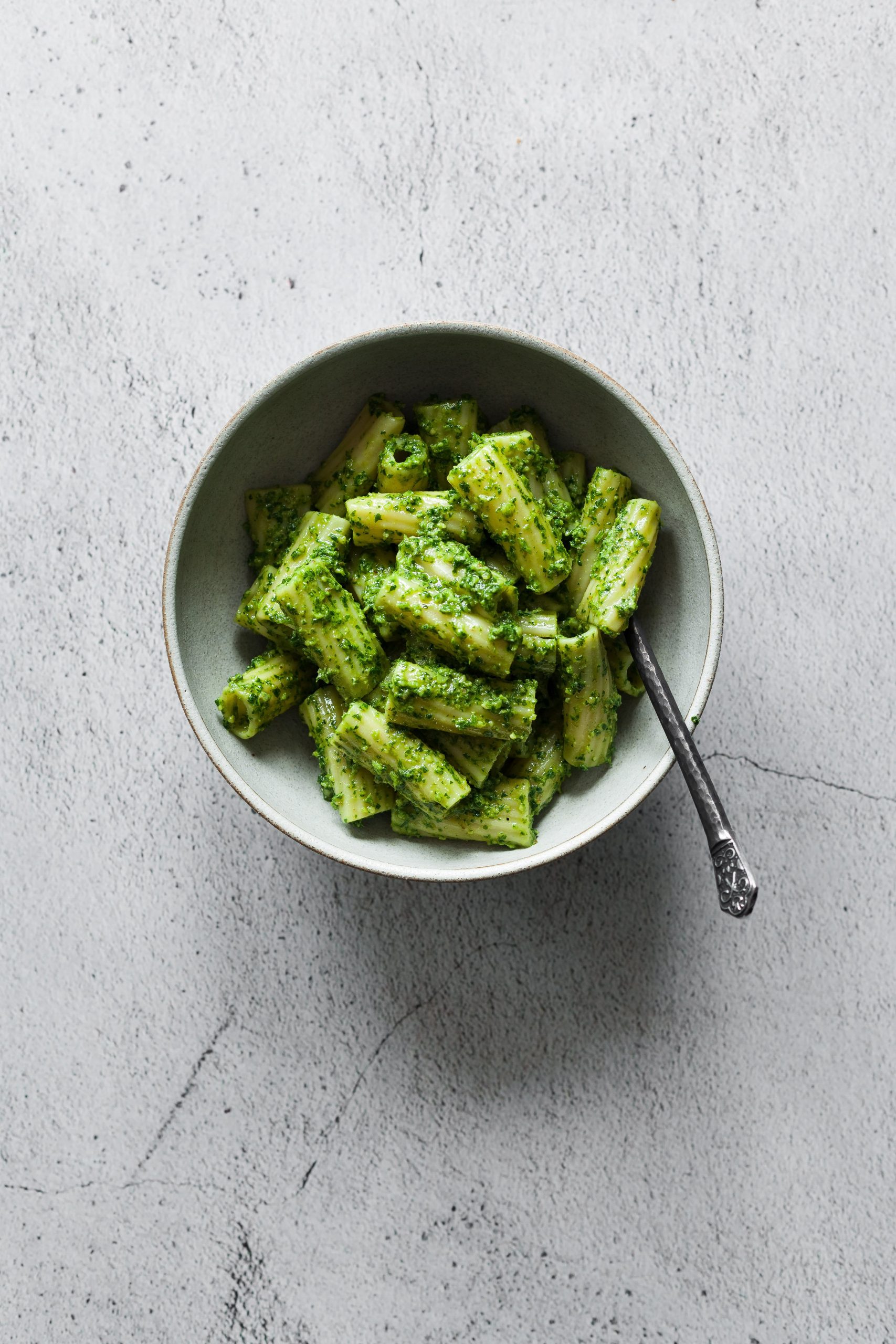 a overhead shot of a bowl of Rigatoni with pesto with a fork.