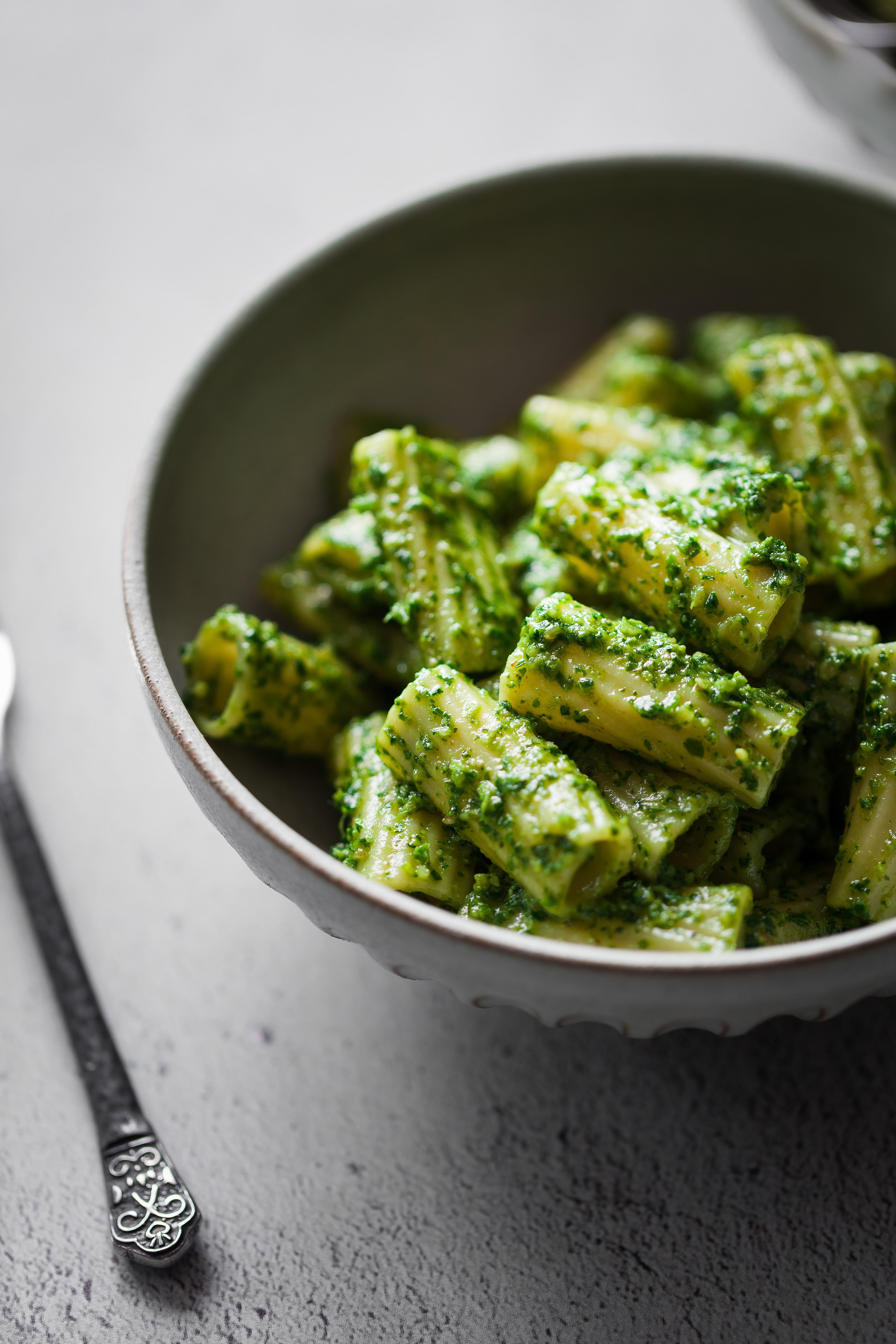 a close up ¾ angle shot of a bowl of pesto pasta on a white stone surface.