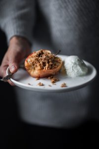 a person holding a white plate with a baked apple and ice cream on it.