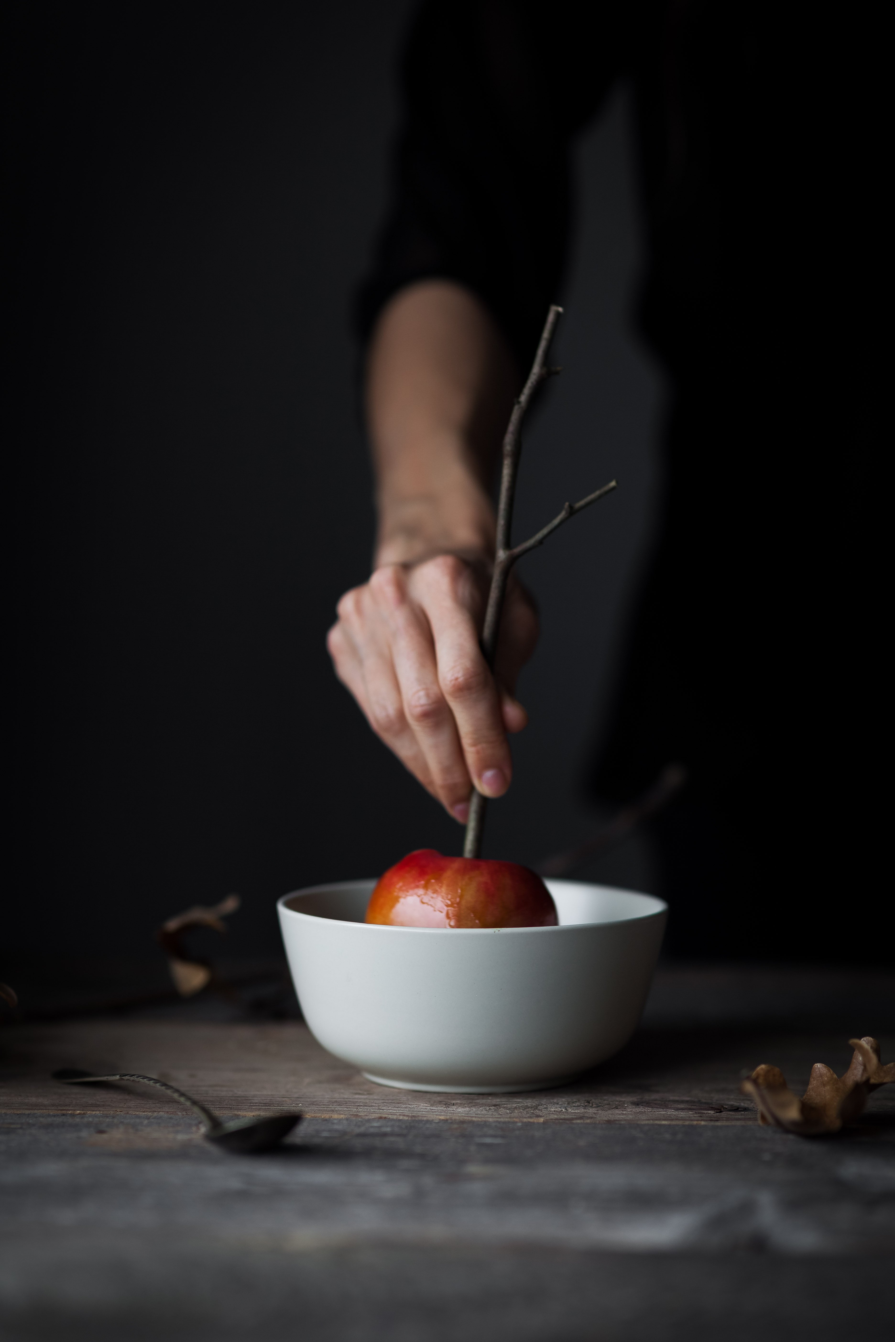 portrait view of a hand holding a caramel apple in a bowl of caramel sauce.
