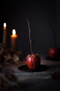 a head on image of a caramel apple on a black plate with candles in the background.