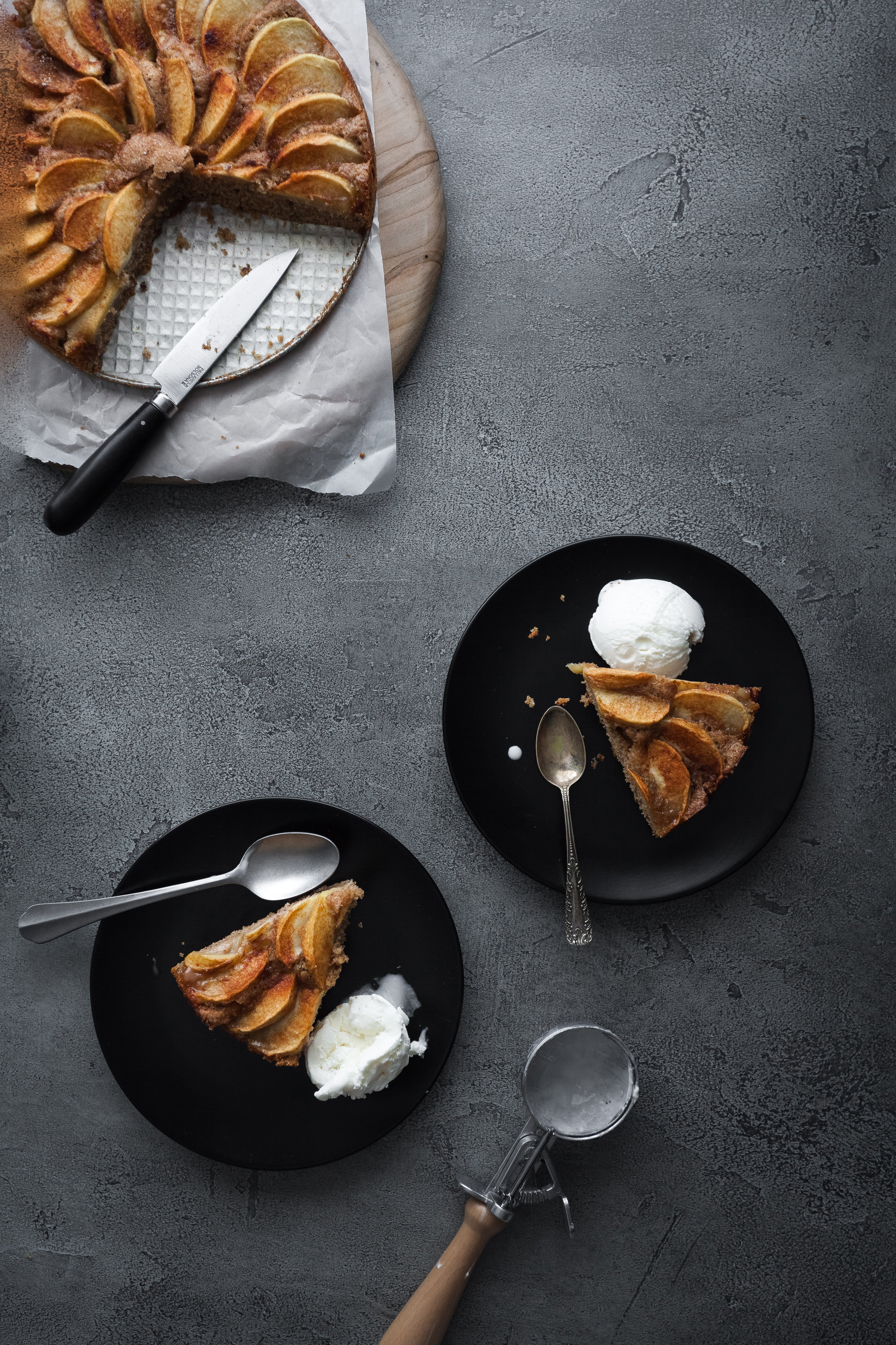 an overhead image of vegan german apple cake with two slices on plates with ice cream.